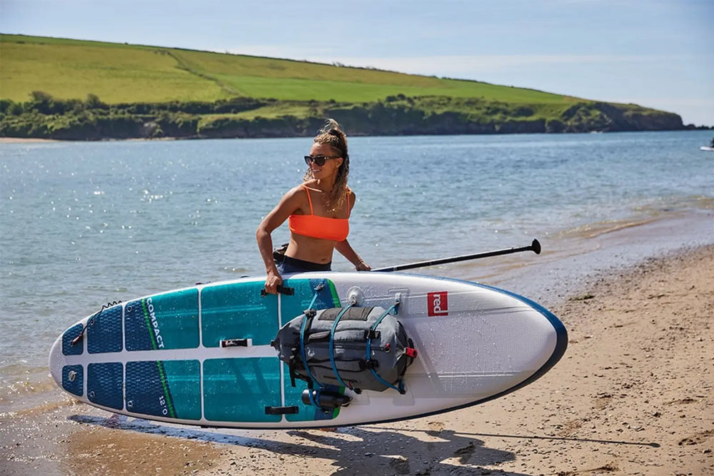 A woman carrying her paddleboard out onto the beach on a sunny day