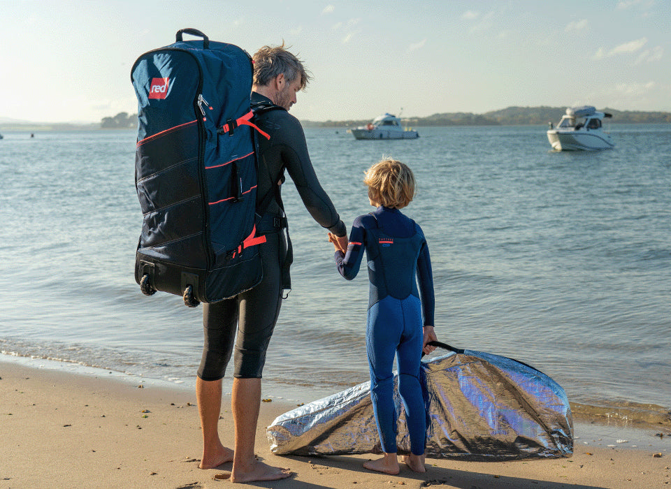 A man holding his sons hand on the beach carrying a backpack 