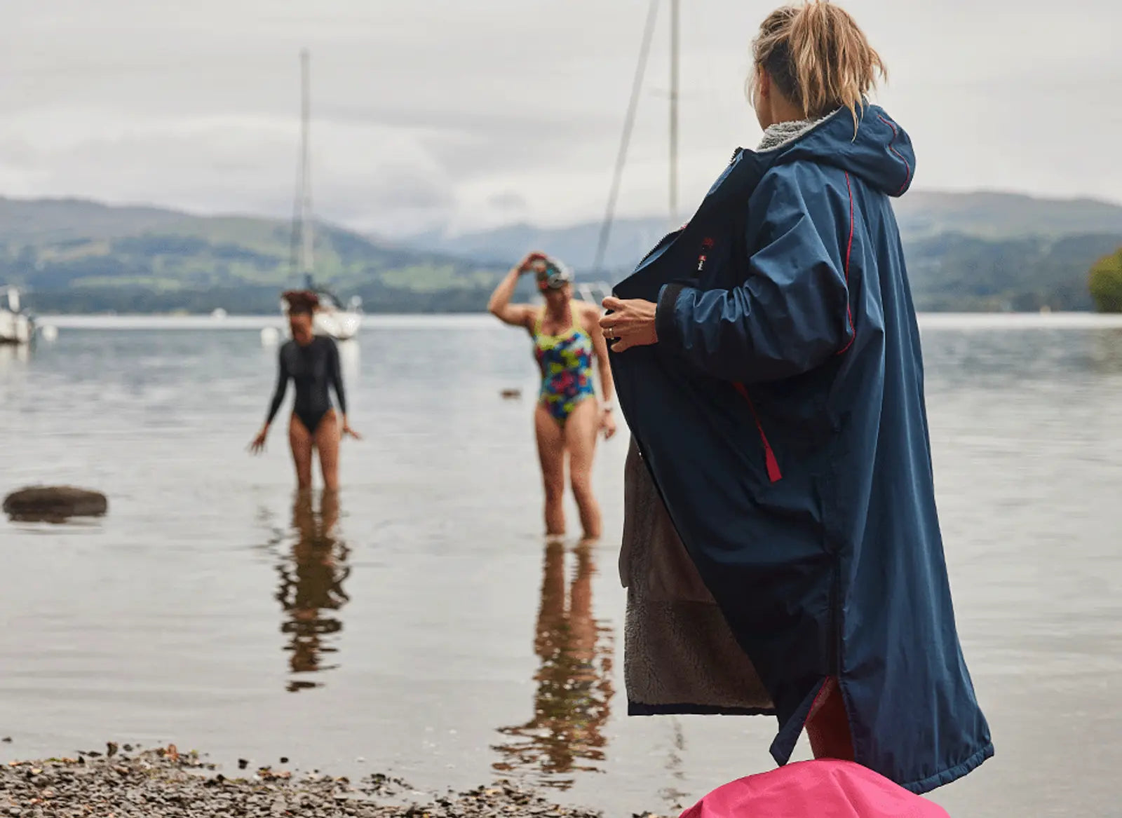 A woman wearing her pro change robe and 2 other women paddling in the sea