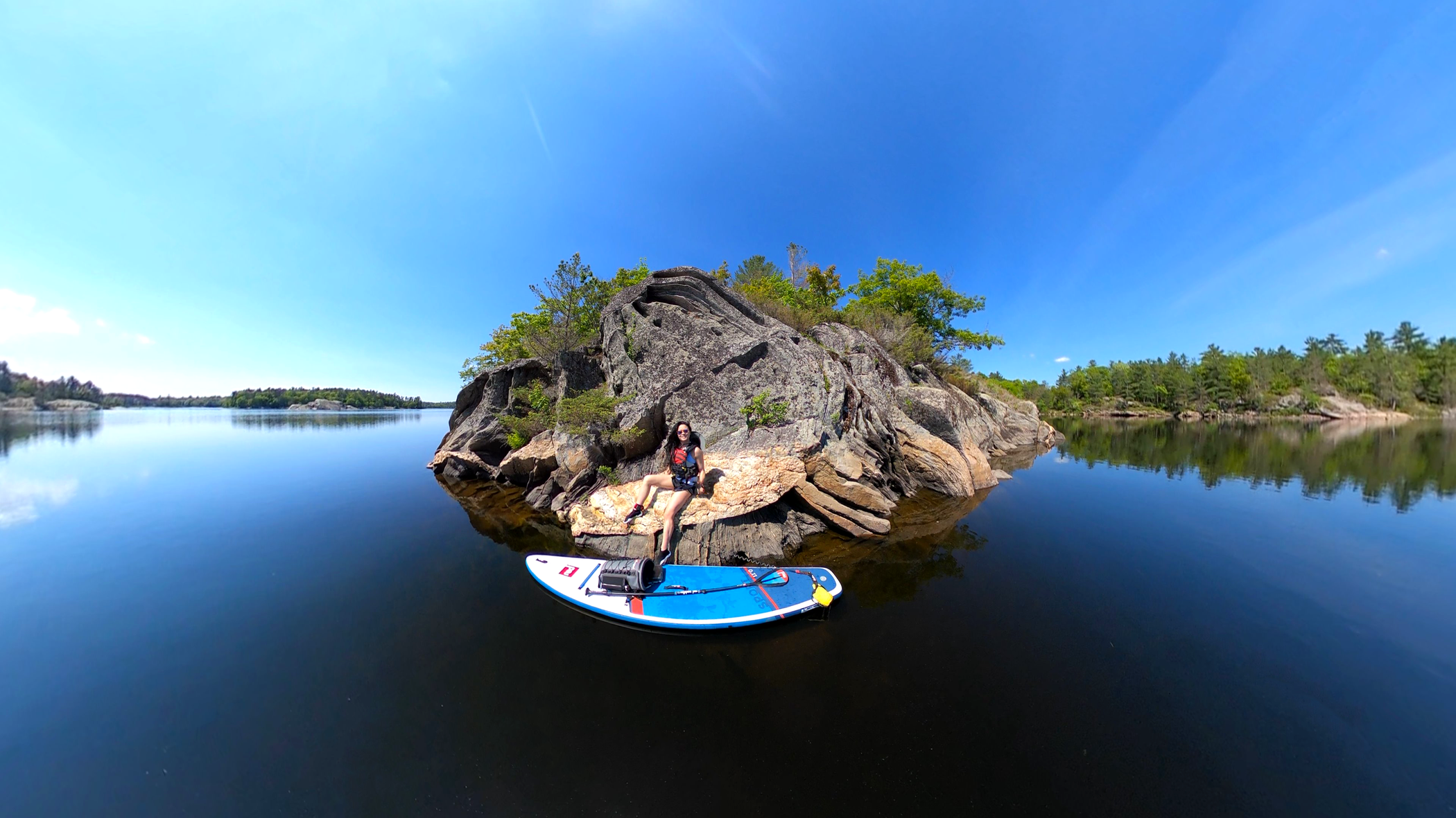Woman sat on rocks in lake with Red Original paddle board