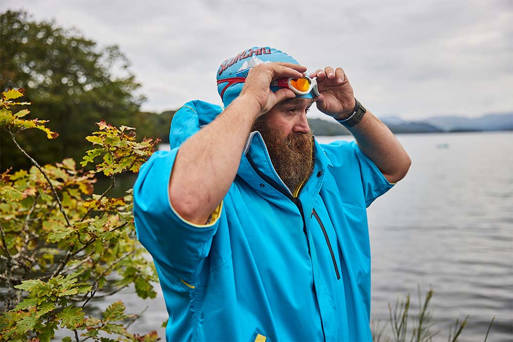 Man stood by the sea wearing Red Original waterproof changing robe and swimming goggles 