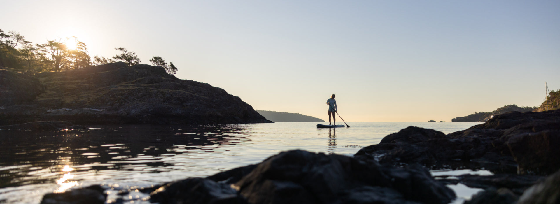 A person paddleboarding out into the ocean during sunset