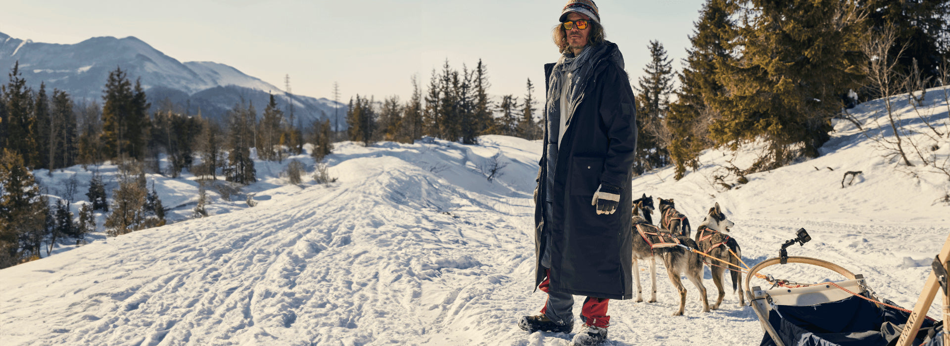 A man hiking through the snow with his dogs pulling a sled