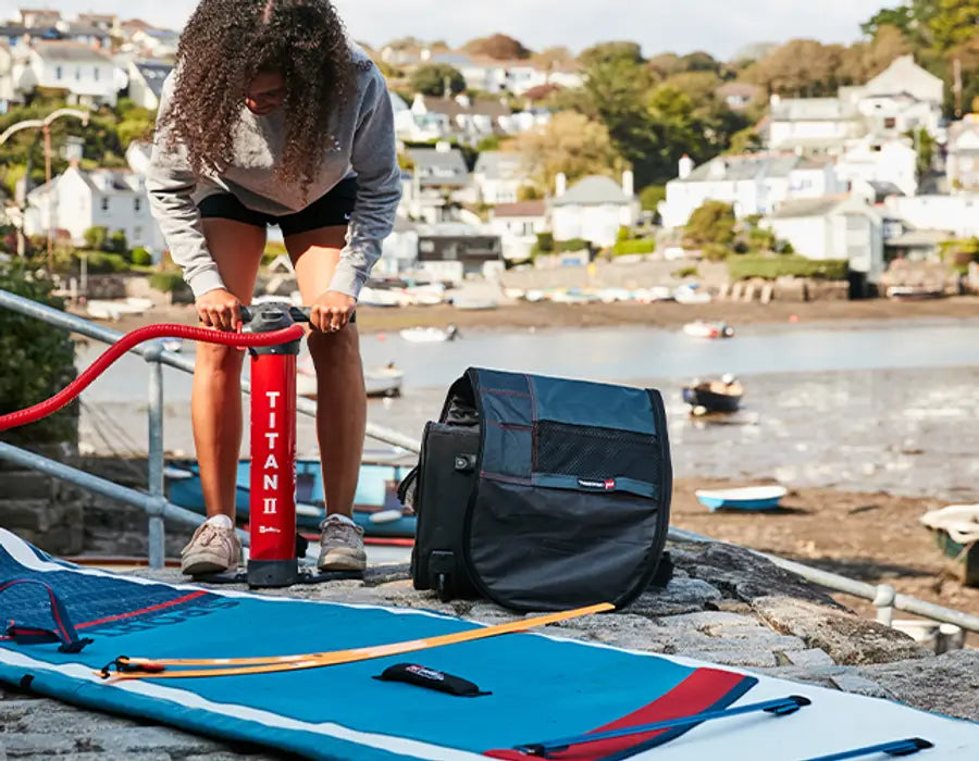 A woman using the Red Titan 2 Pump for her paddleboard by the water