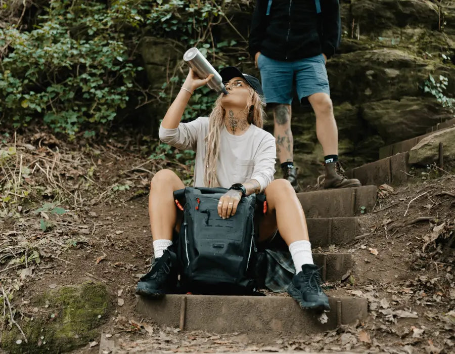 person next to backpack drinking bottle of water