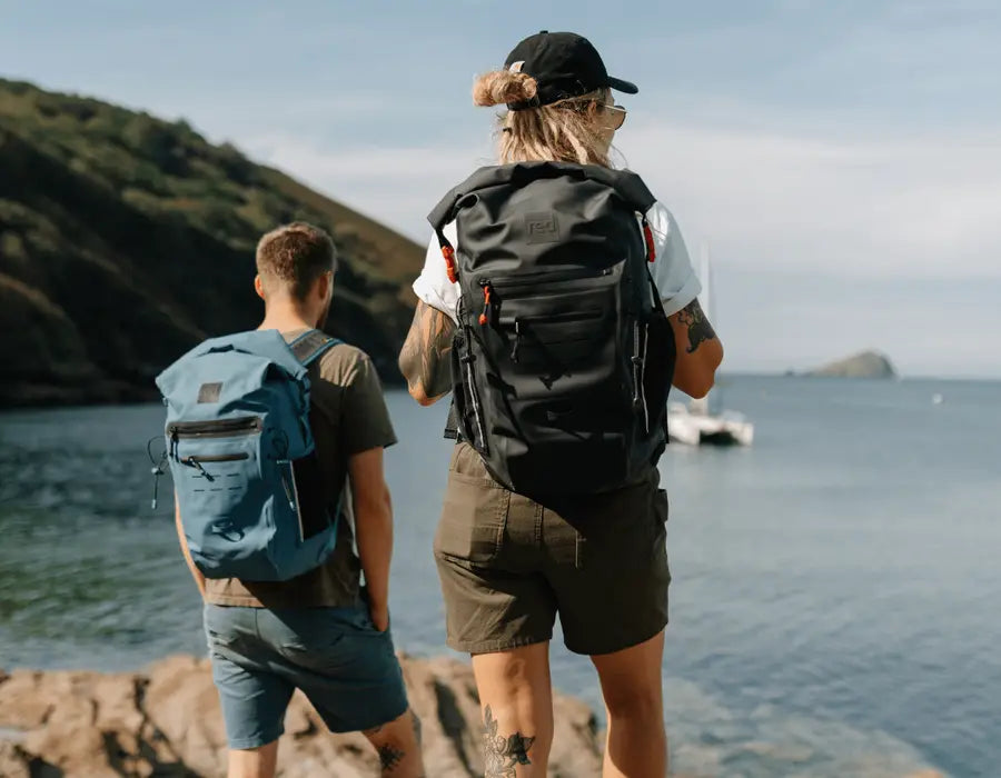 2 people carrying the Red adventure backpack, looking out to sea