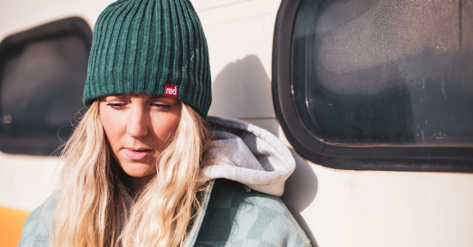 woman wearing teal knitted beanie standing next to a campervan