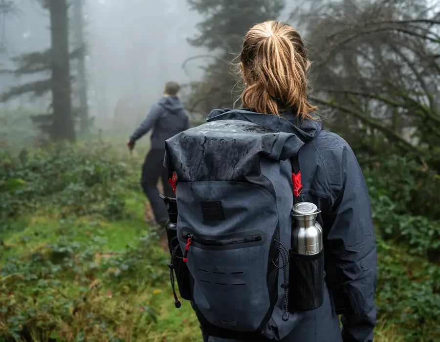 A woman wearing a waterproof backpack whilst walking in the forest in the rain