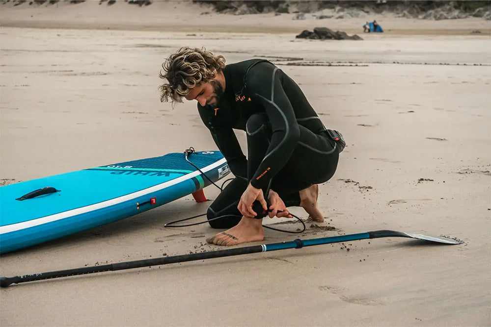 A man attaching his paddleboard safety strap to to his ankle on the beach