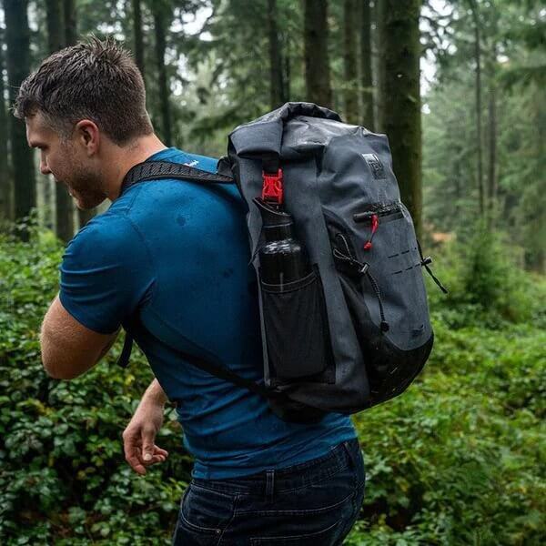 man carrying Red Original Waterproof Backpack whilst walking through a woodland area