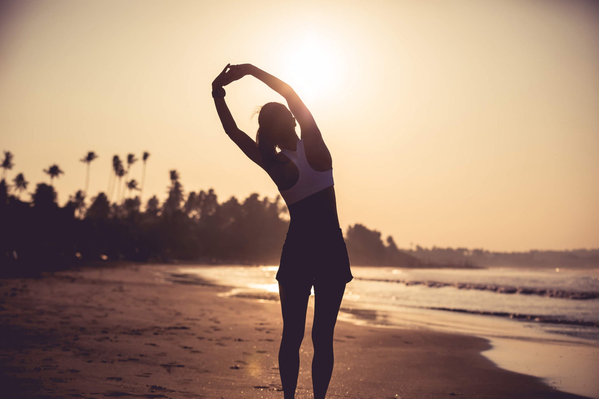 woman doing an overhead stretch on a beach at sun rise