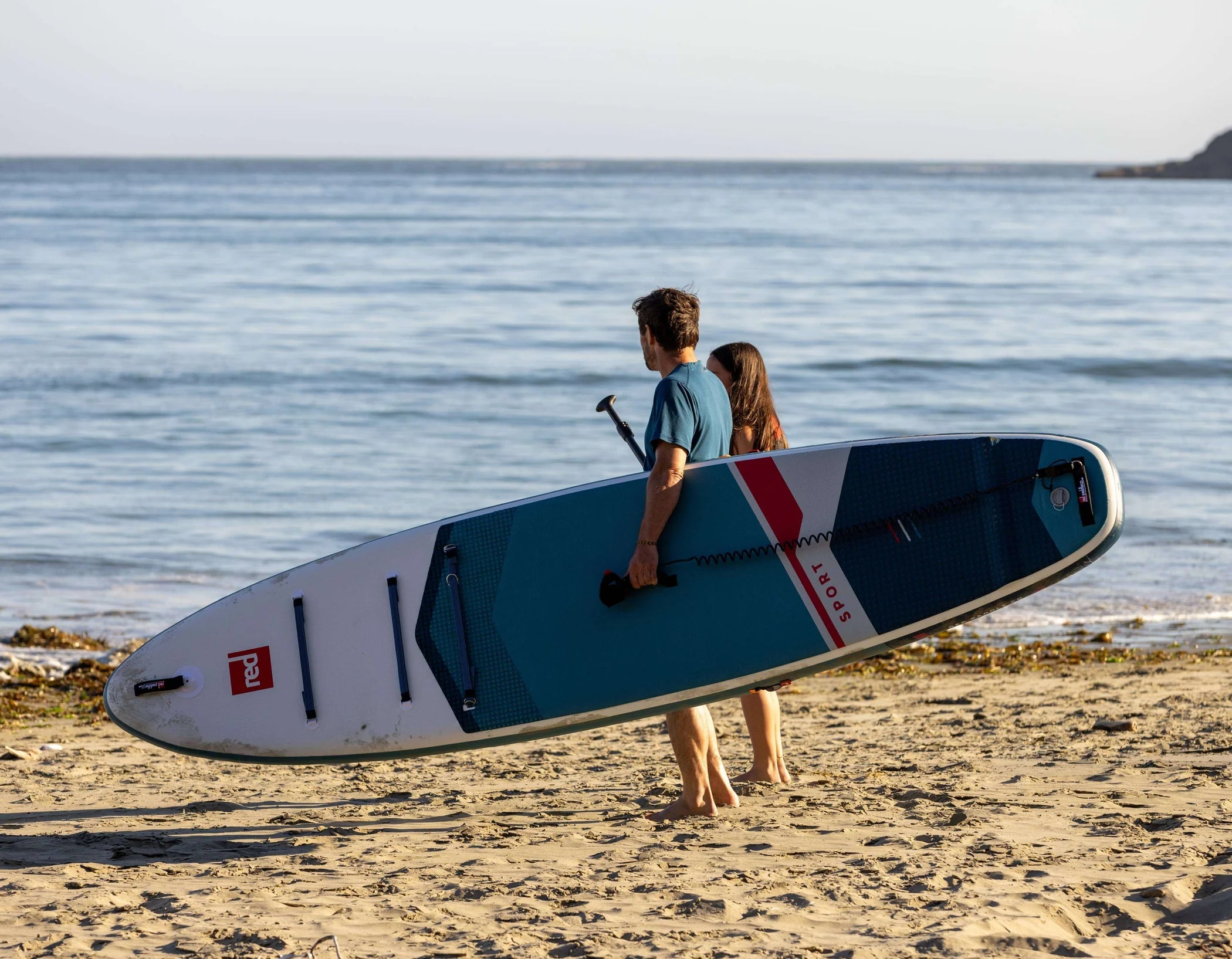 A man and woman walking along a beach carrying their paddleboard