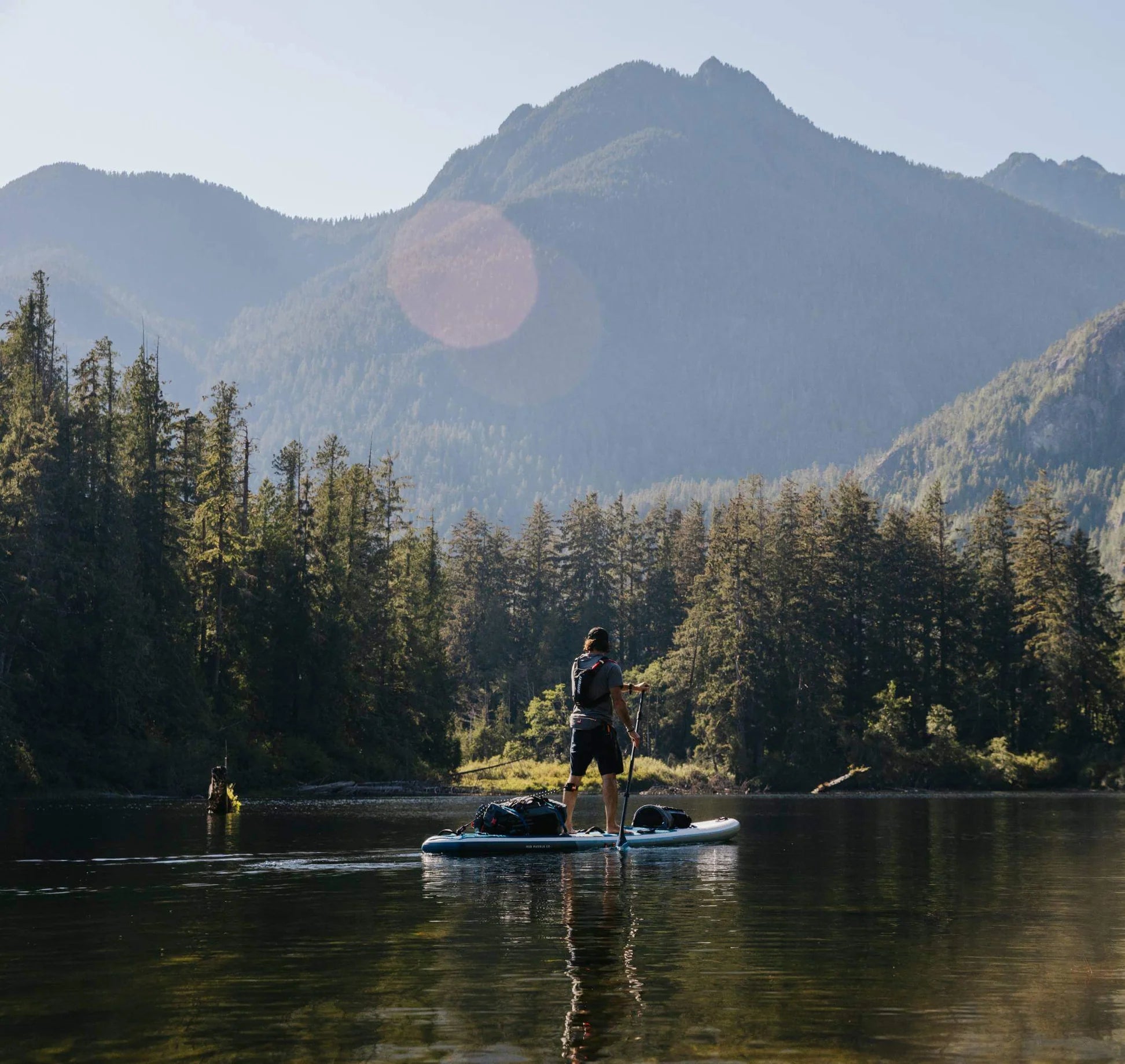 A man paddleboard in a lake with a surrounding of a forest and hills