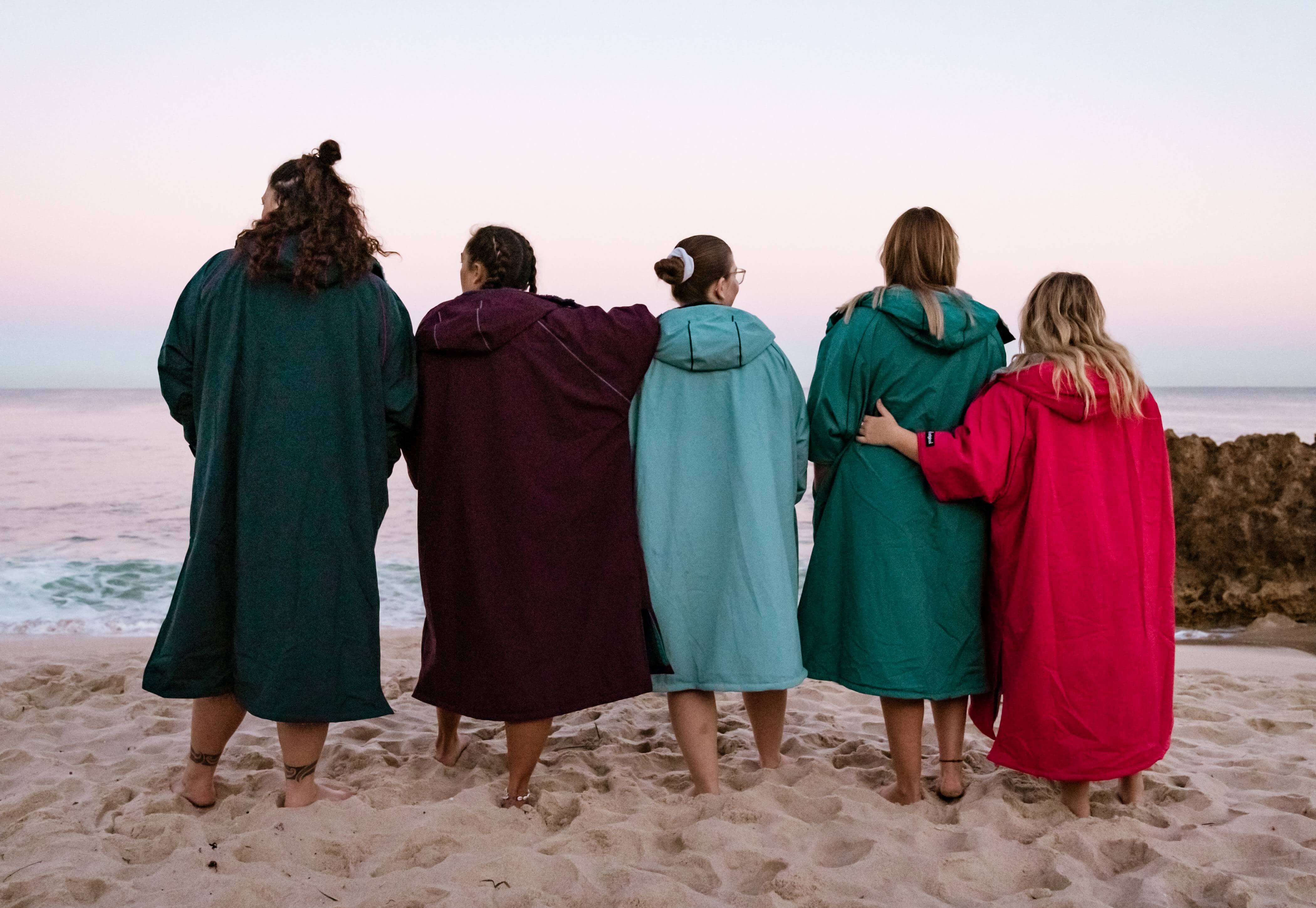 Five women standing on the beach wearing Red Pro Change Robe Evo.