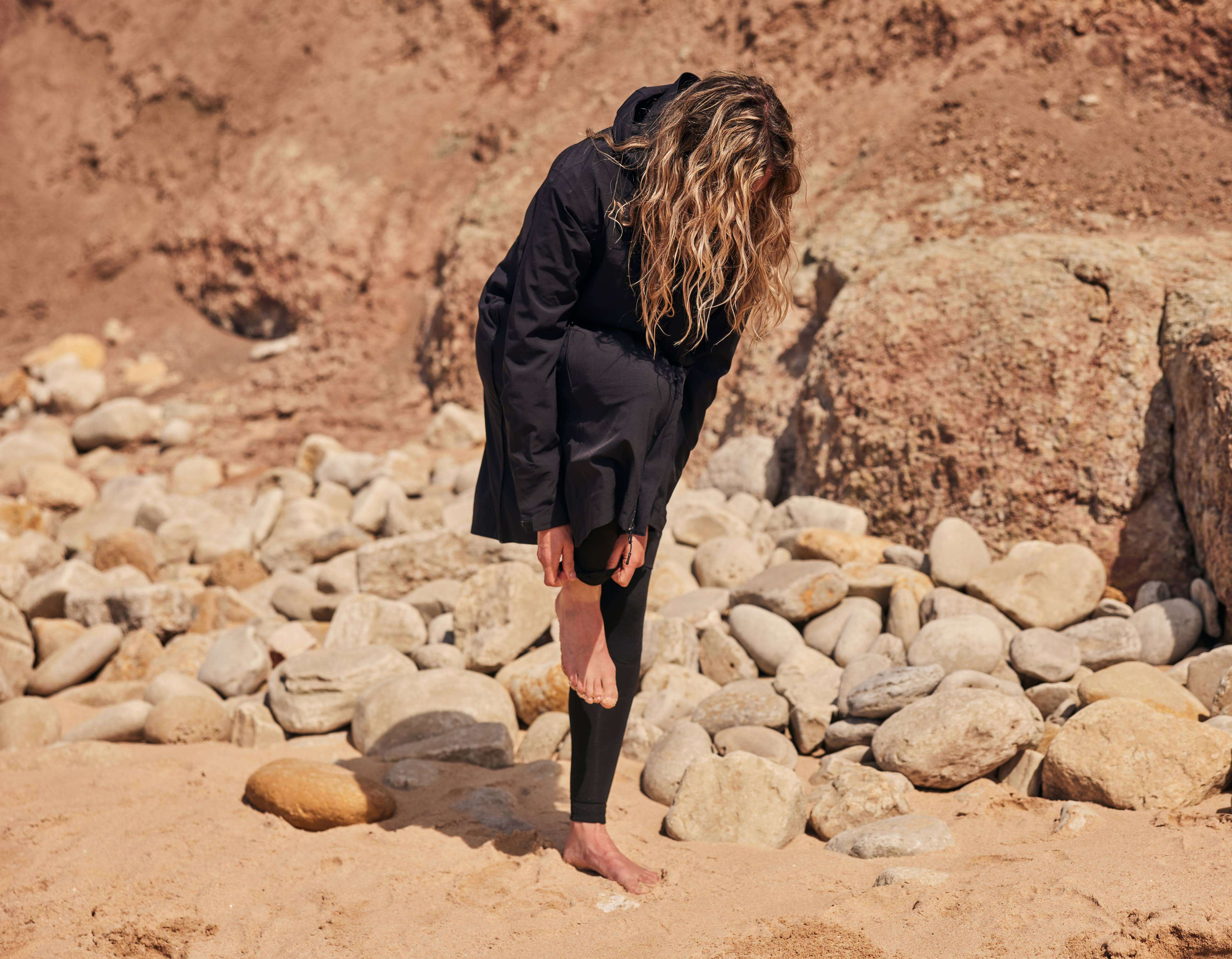 Woman changing on the beach wearing a Red Pursuit Waterproof Lightweight Changing Robe Jacket in Obsidian Black.